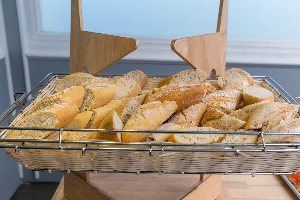 A French bakery counter with various breads, focusing on a baguette placed upside-down, with subtle signs of unease from nearby people