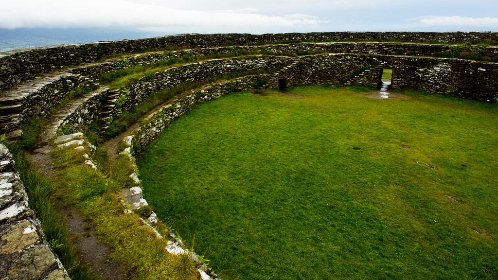 A misty Irish landscape with an ancient circular fairy fort surrounded by lush green grass and wildflowers